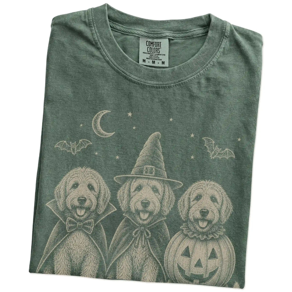 Folded Moss Comfort Colors® T-shirt showing three Labradoodle dogs dressed for Halloween beneath bats and a crescent moon