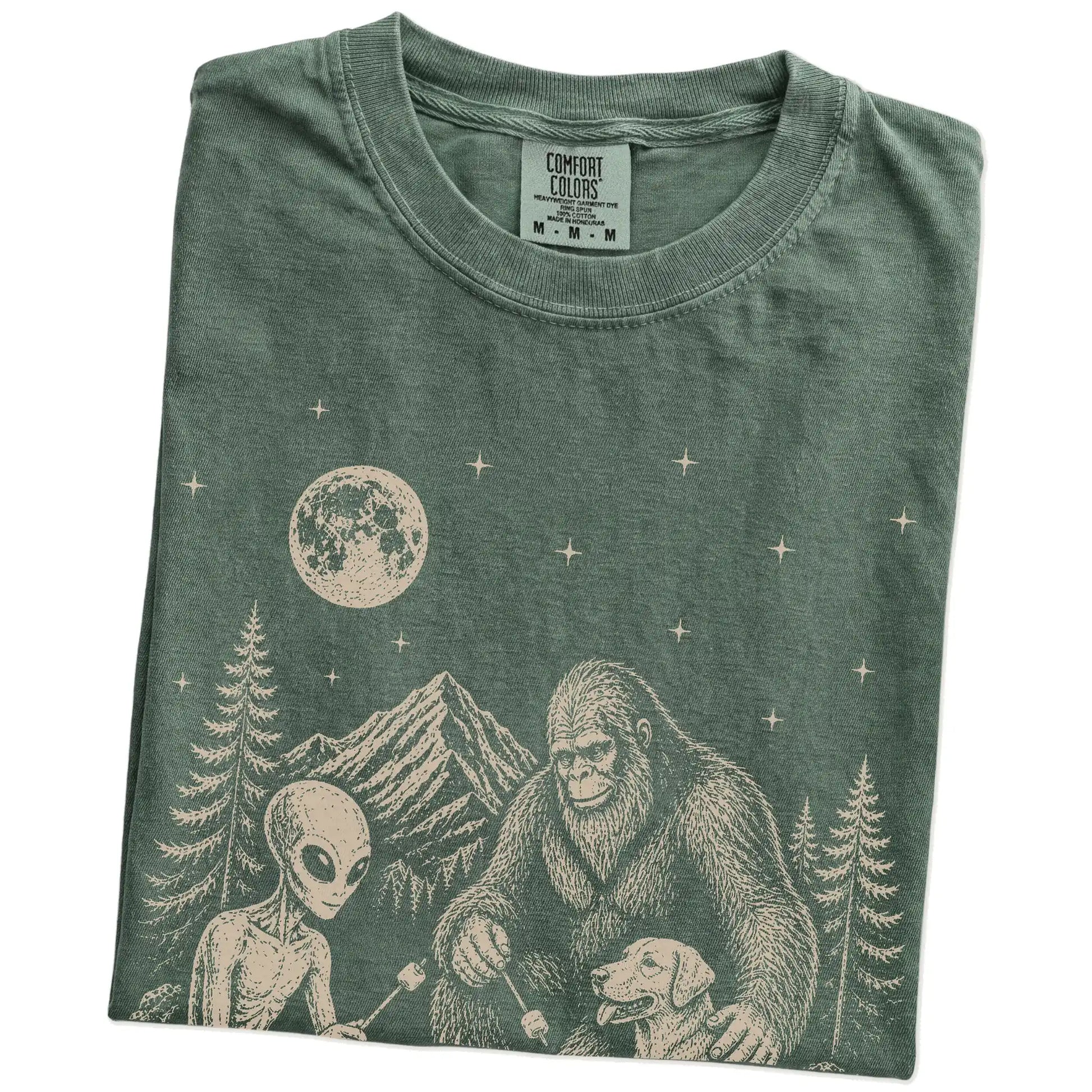 Folded Moss Comfort Colors® T-shirt showing Labrador Retriever camping with Bigfoot and an alien