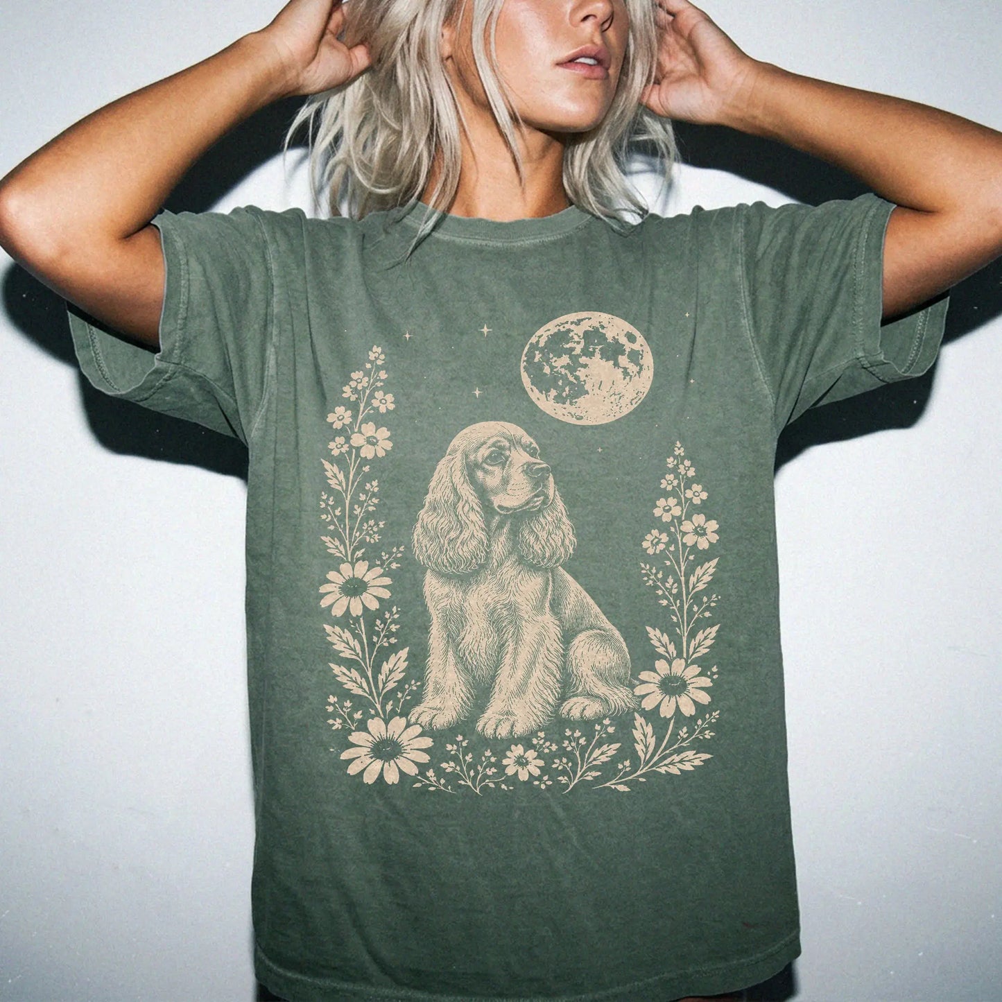Model wearing a Moss Comfort Colors® T-shirt featuring Cocker Spaniel framed by flowers beneath the moon