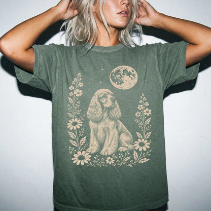 Model wearing a Moss Comfort Colors® T-shirt featuring Cocker Spaniel framed by flowers beneath the moon