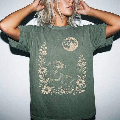 Model wearing a Moss Comfort Colors® T-shirt featuring Dachshund framed by flowers beneath the moon
