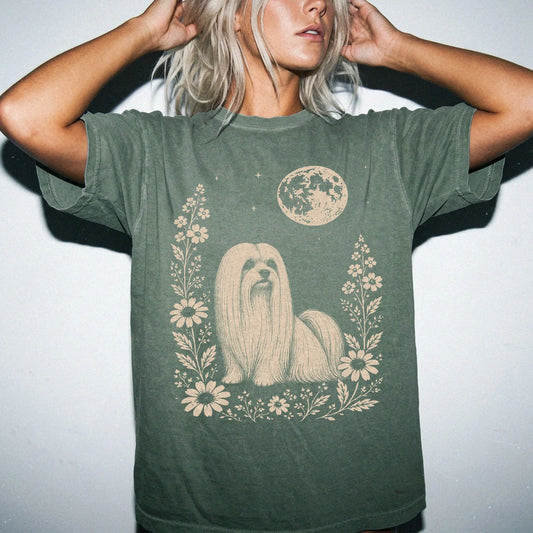 Model wearing a Moss Comfort Colors® T-shirt featuring Maltese framed by flowers beneath the moon