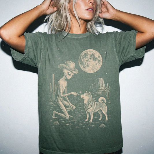 Model wearing a Moss Comfort Colors® T-shirt with cowboy alien fist-bumping a shiba inu beneath the moon
