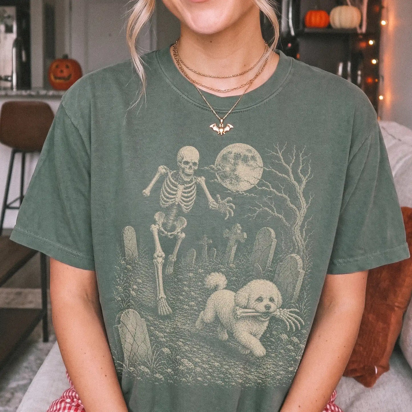 Model wearing a Moss Comfort Colors® T-shirt showing Bichon Frise running through a moonlit graveyard with a chasing skeleton
