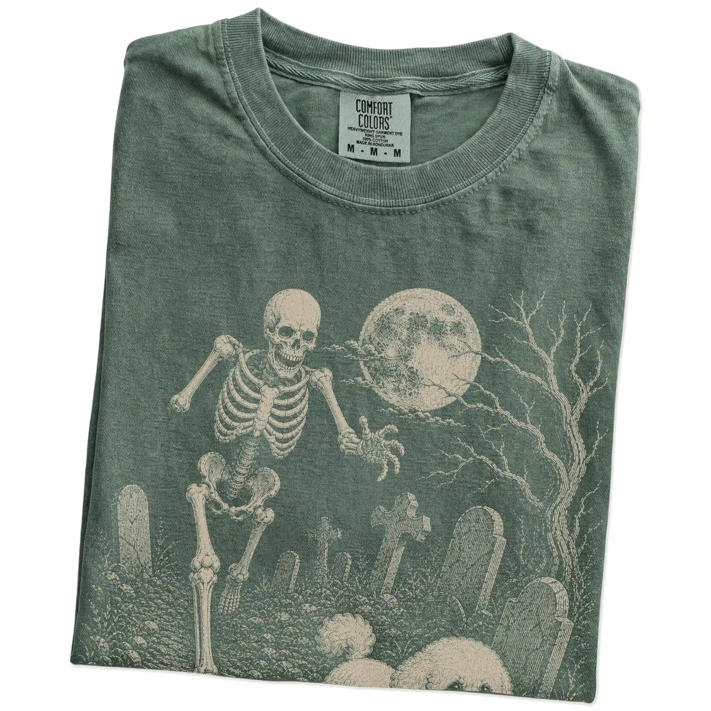 Folded Moss Comfort Colors® T-shirt showing Bichon Frise running through a moonlit graveyard with a chasing skeleton