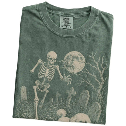 Folded Moss Comfort Colors® T-shirt showing Bichon Frise running through a moonlit graveyard with a chasing skeleton