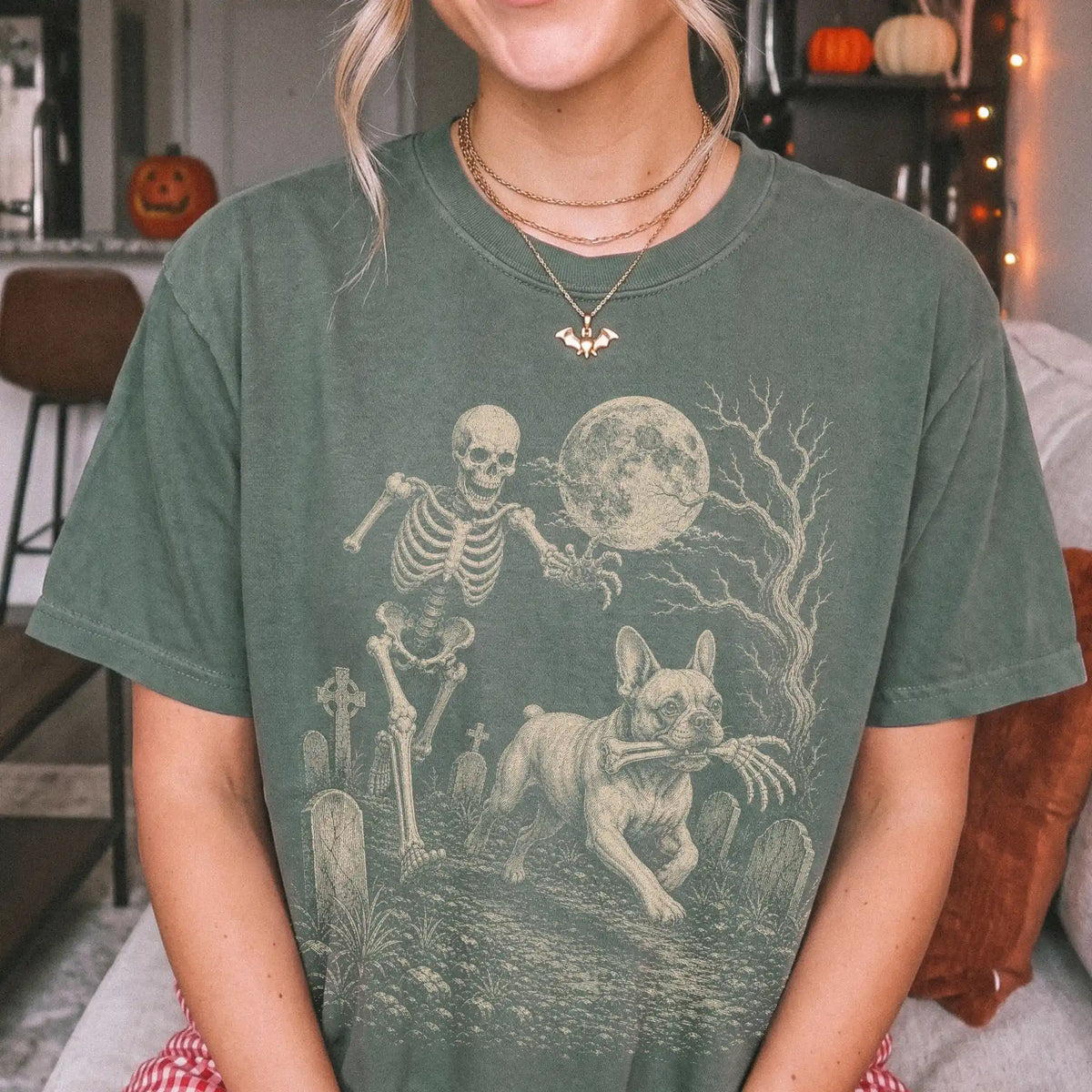Model wearing a Moss Comfort Colors® T-shirt showing French Bulldog running through a moonlit graveyard with a chasing skelet