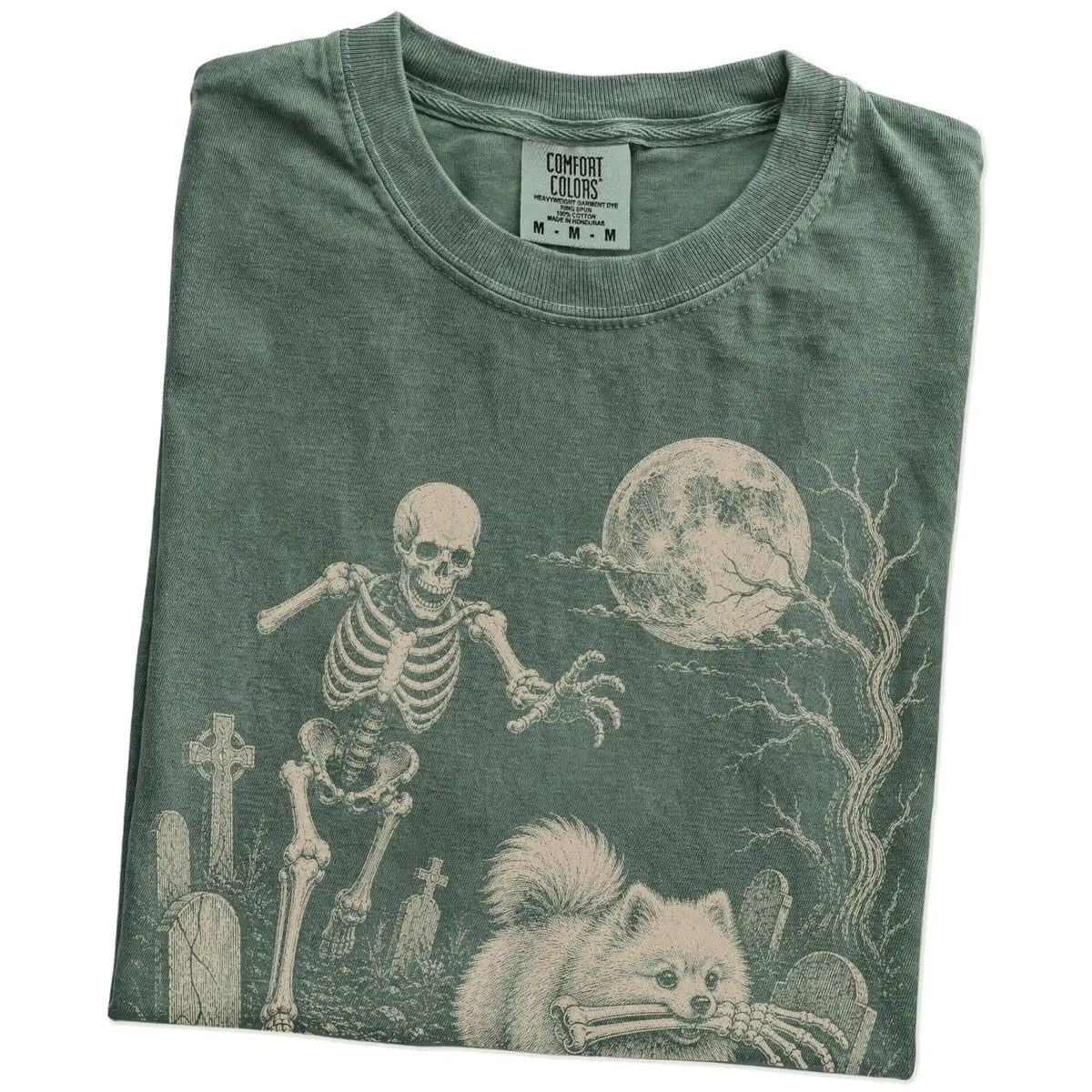 Folded Moss Comfort Colors® T-shirt showing Pomeranian running through a moonlit graveyard with a chasing skeleton