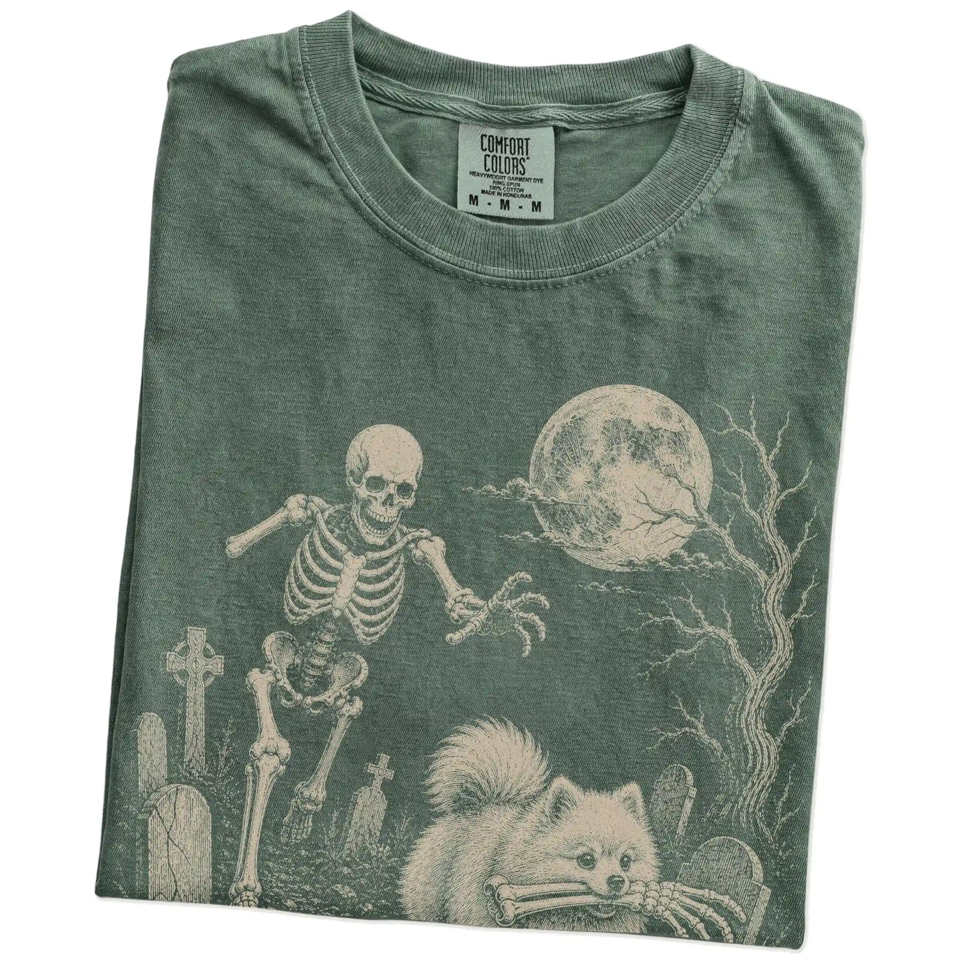 Folded Moss Comfort Colors® T-shirt showing Pomeranian running through a moonlit graveyard with a chasing skeleton