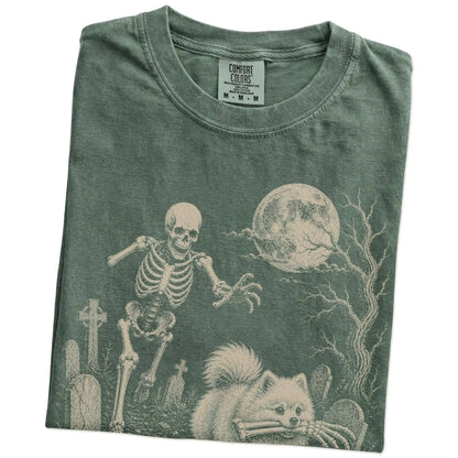 Folded Moss Comfort Colors® T-shirt showing Pomeranian running through a moonlit graveyard with a chasing skeleton