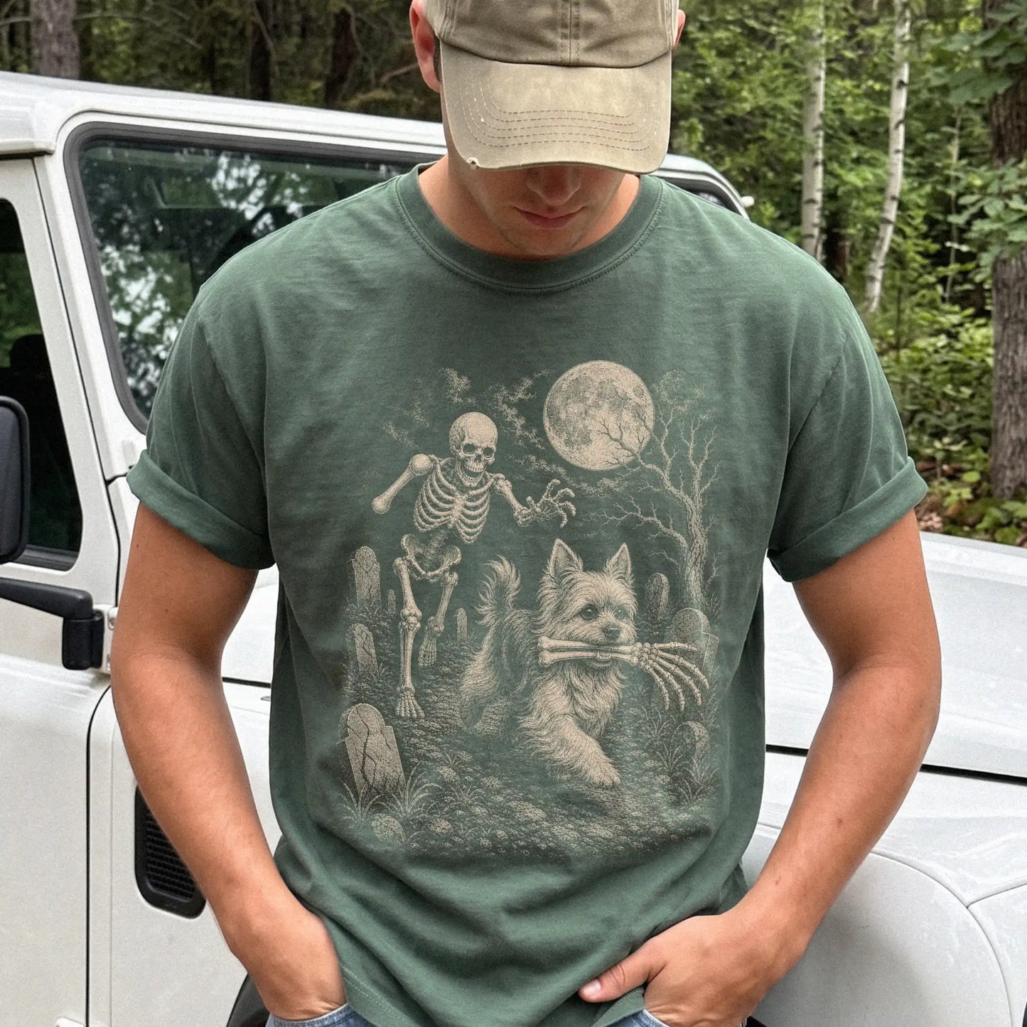 Model wearing a Moss Comfort Colors® T-shirt showing Yorkie running through a moonlit graveyard with a chasing skeleton