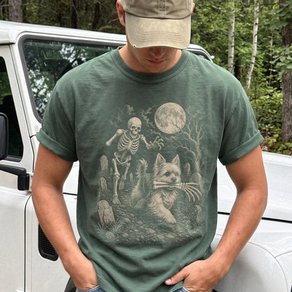 Model wearing a Moss Comfort Colors® T-shirt showing Yorkie running through a moonlit graveyard with a chasing skeleton