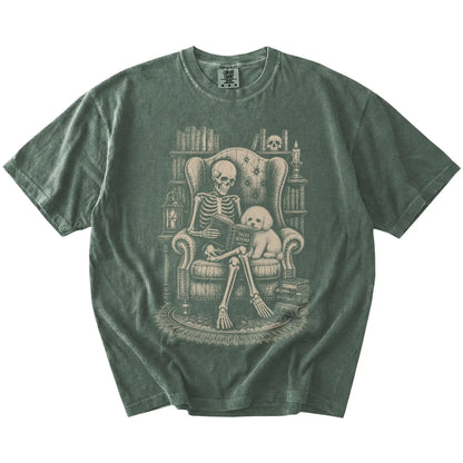 Skeleton reading in a library beside a Bichon Frise on a Moss Comfort Colors® T-shirt