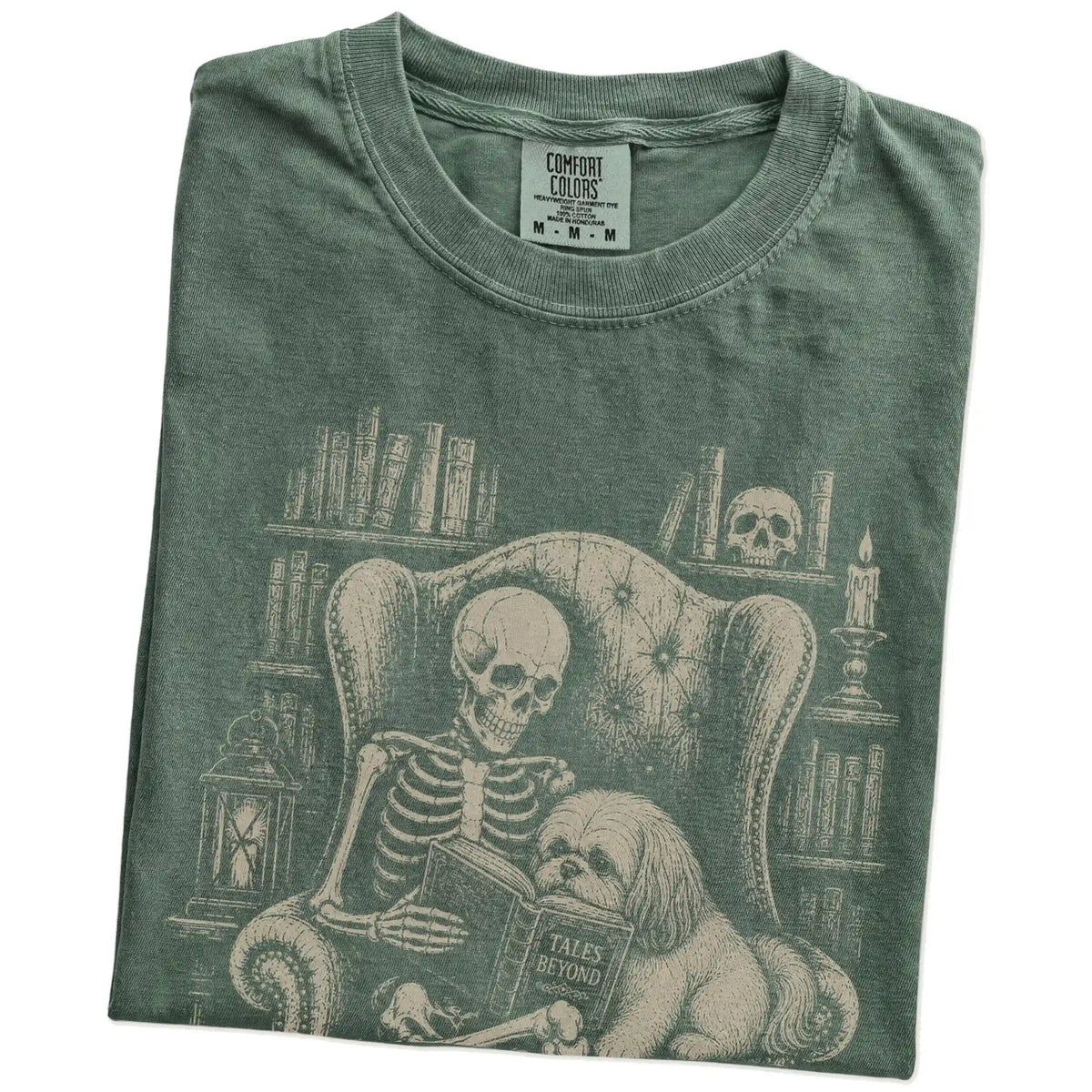 Folded Moss Comfort Colors® T-shirt showing skeleton reading in a library beside a Shih Tzu