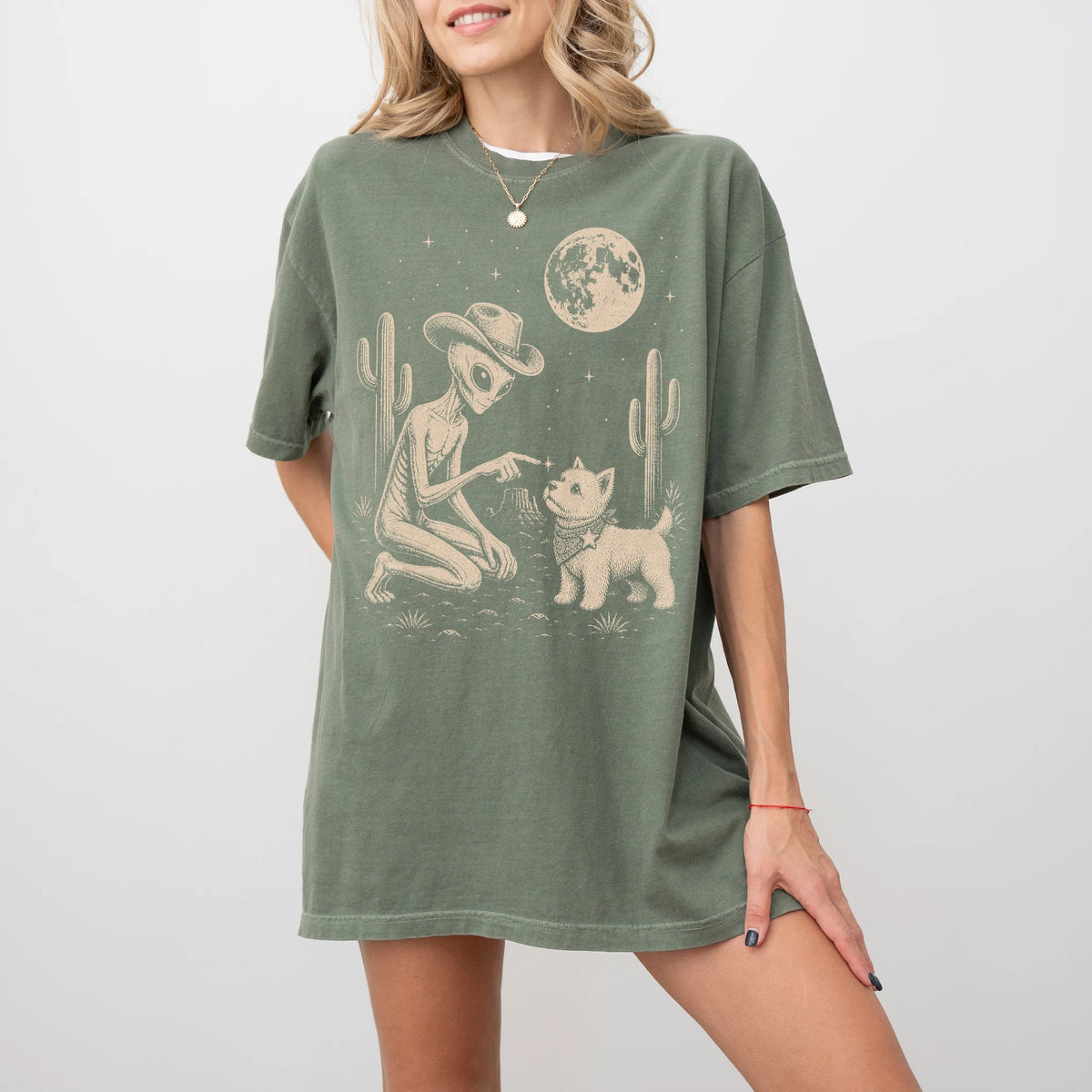 Model wearing a Moss Comfort Colors® T-shirt with cowboy alien fist-bumping a westie beneath the moon