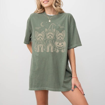 Model wearing a Moss Comfort Colors® T-shirt showing three Yorkie dogs dressed for Halloween beneath bats and a crescent moon