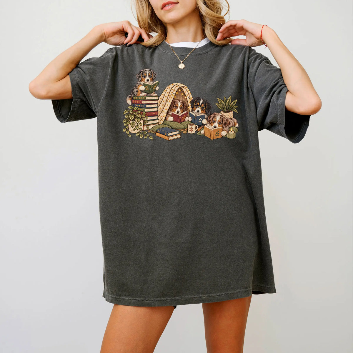 Australian Shepherd puppies reading books in a cozy blanket fort on a Pepper T-shirt worn by a model