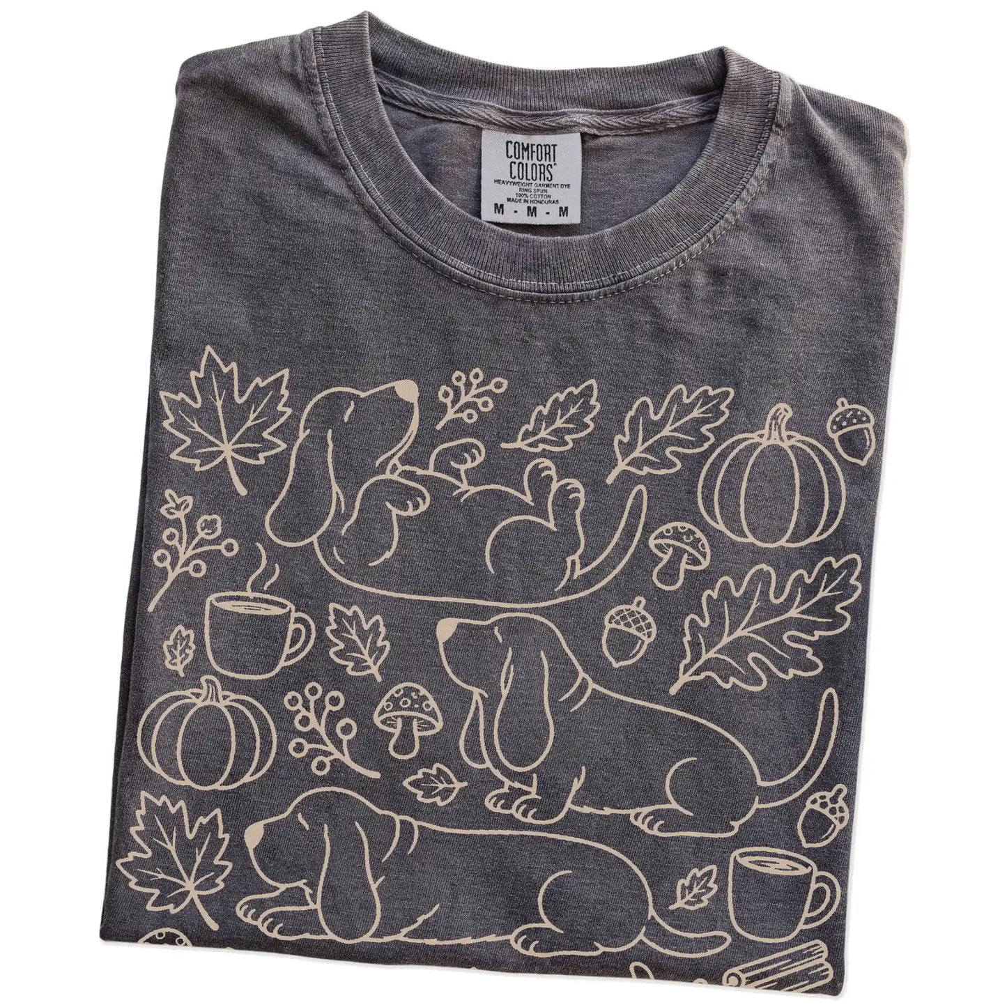 Folded Pepper Comfort Colors® T-shirt showing Basset Hound dogs with pumpkins, leaves, acorns, and woodland details