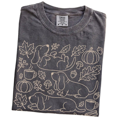 Folded Pepper Comfort Colors® T-shirt showing Basset Hound dogs with pumpkins, leaves, acorns, and woodland details