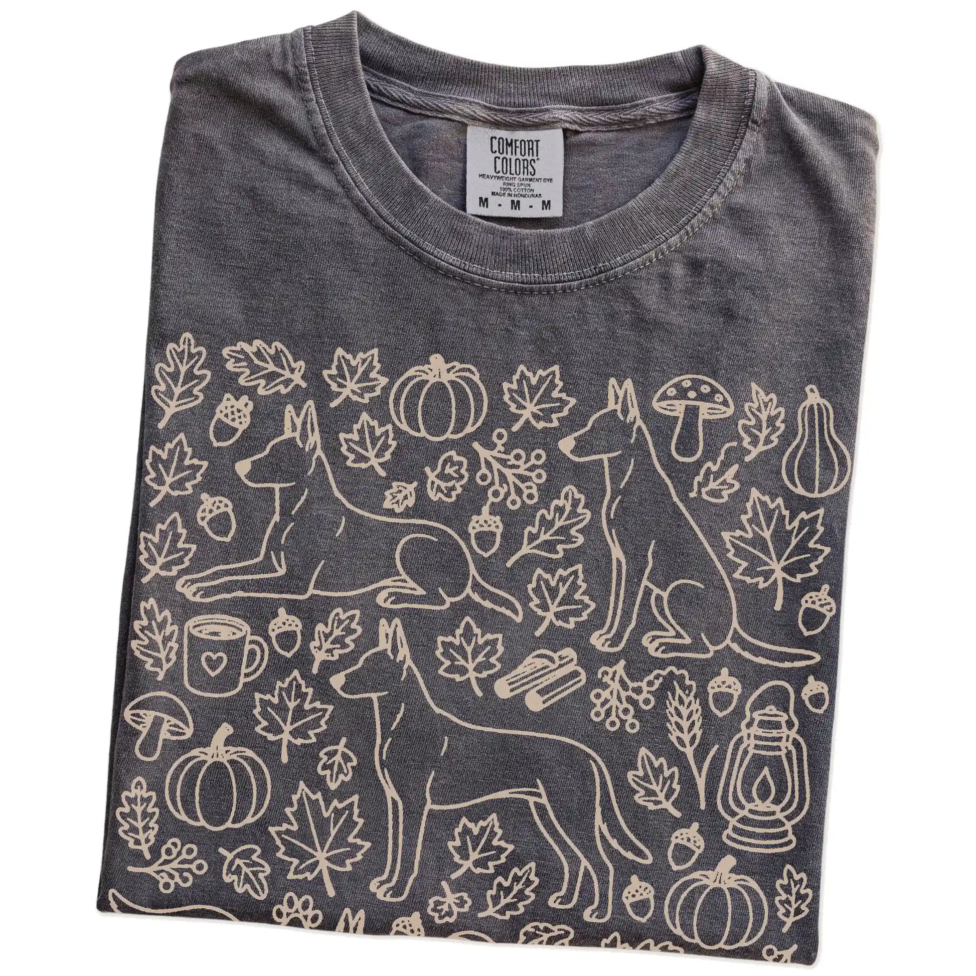 Folded Pepper Comfort Colors® T-shirt showing Belgian Malinois dogs with pumpkins, leaves, acorns, and woodland details