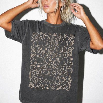 Model wearing a Pepper Comfort Colors® T-shirt with Boston Terrier dogs with pumpkins, leaves, acorns, and woodland details