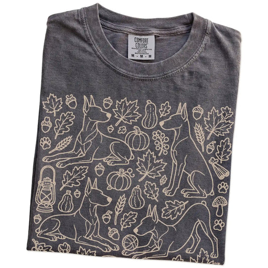 Folded Pepper Comfort Colors® T-shirt showing Doberman dogs with pumpkins, leaves, acorns, and woodland details