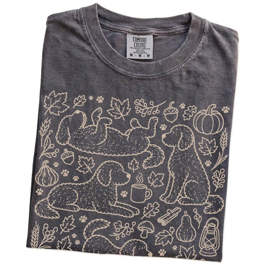 Folded Pepper Comfort Colors® T-shirt showing Labradoodle dogs with pumpkins, leaves, acorns, and woodland details