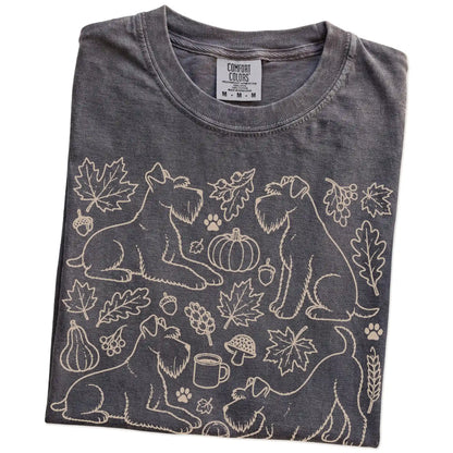 Folded Pepper Comfort Colors® T-shirt showing Schnauzer dogs with pumpkins, leaves, acorns, and woodland details