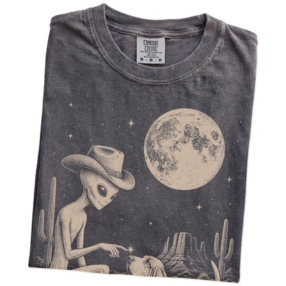 Folded Pepper Comfort Colors® T-shirt showing cowboy alien fist-bumping a basset hound beneath the moon