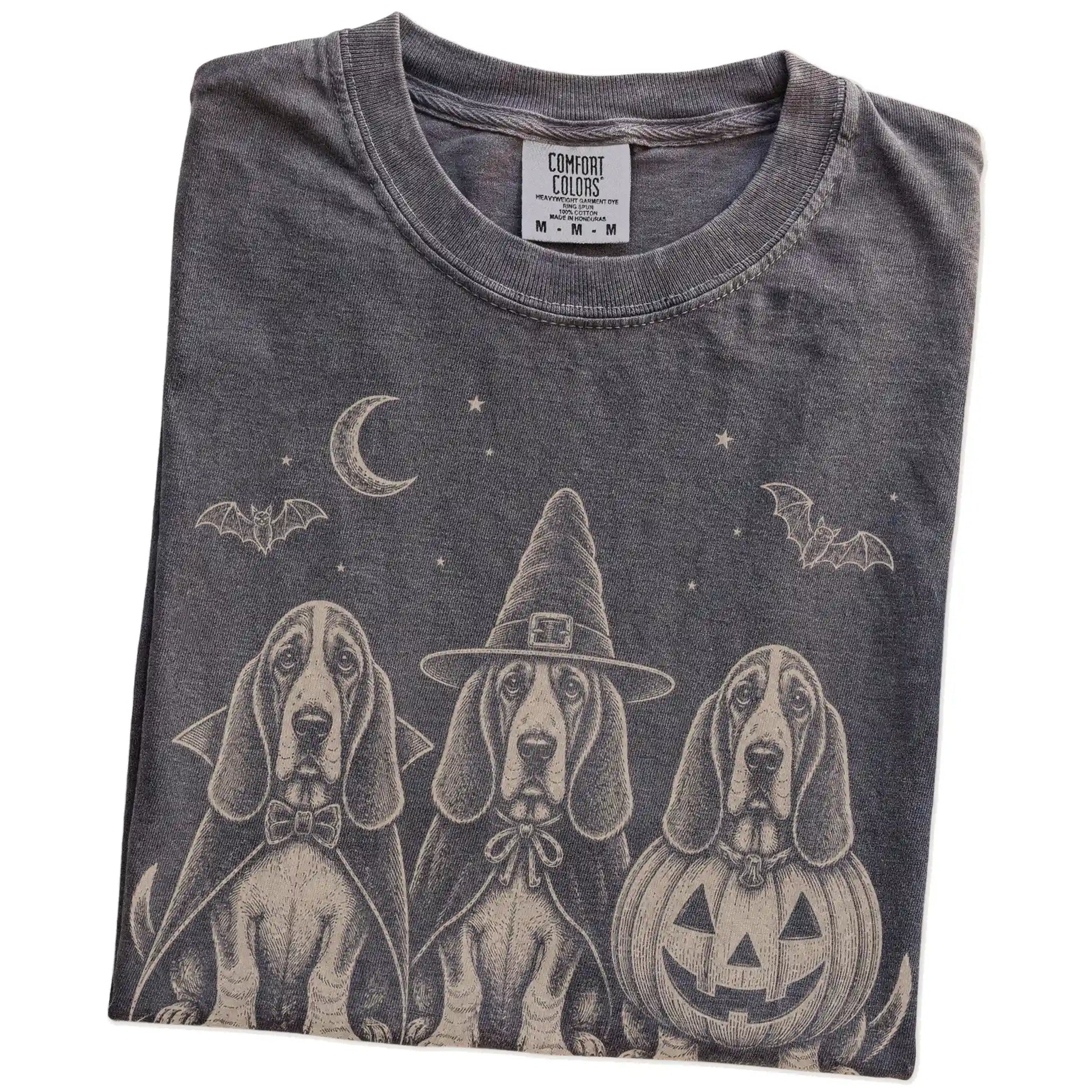 Folded Pepper Comfort Colors® T-shirt showing three Basset Hound dogs dressed for Halloween beneath bats and a crescent moon