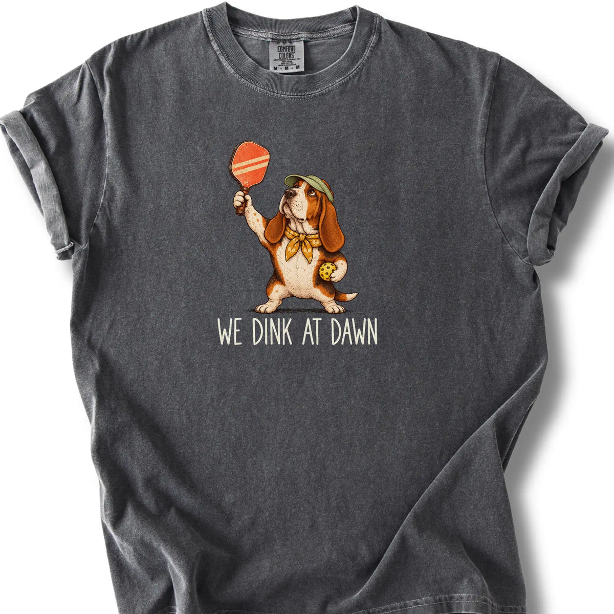 Basset Hound with a pickleball paddle and ball on a Pepper Comfort Colors® T-shirt with We Dink at Dawn text