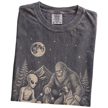 Folded Pepper Comfort Colors® T-shirt showing Belgian Malinois camping with Bigfoot and an alien