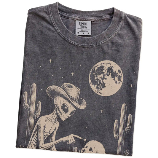 Folded Pepper Comfort Colors® T-shirt showing cowboy alien fist-bumping a bichon frise beneath the moon