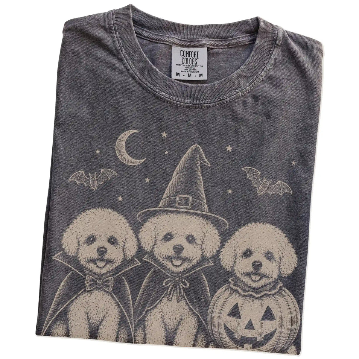 Folded Pepper Comfort Colors® T-shirt showing three Bichon Frise dogs dressed for Halloween beneath bats and a crescent moon