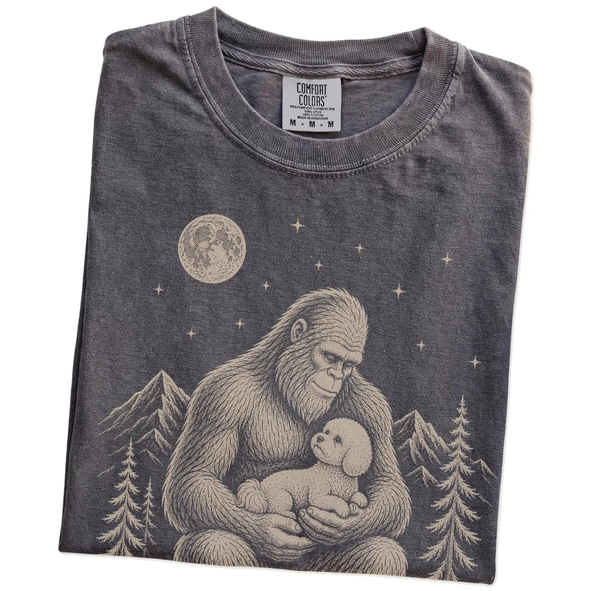 Folded Pepper Comfort Colors® T-shirt showing Bigfoot holding a Bichon Frise