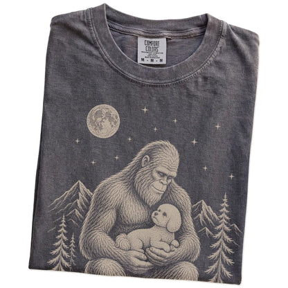 Folded Pepper Comfort Colors® T-shirt showing Bigfoot holding a Bichon Frise