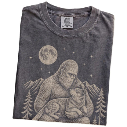 Folded Pepper Comfort Colors® T-shirt showing Bigfoot holding a Blue Heeler