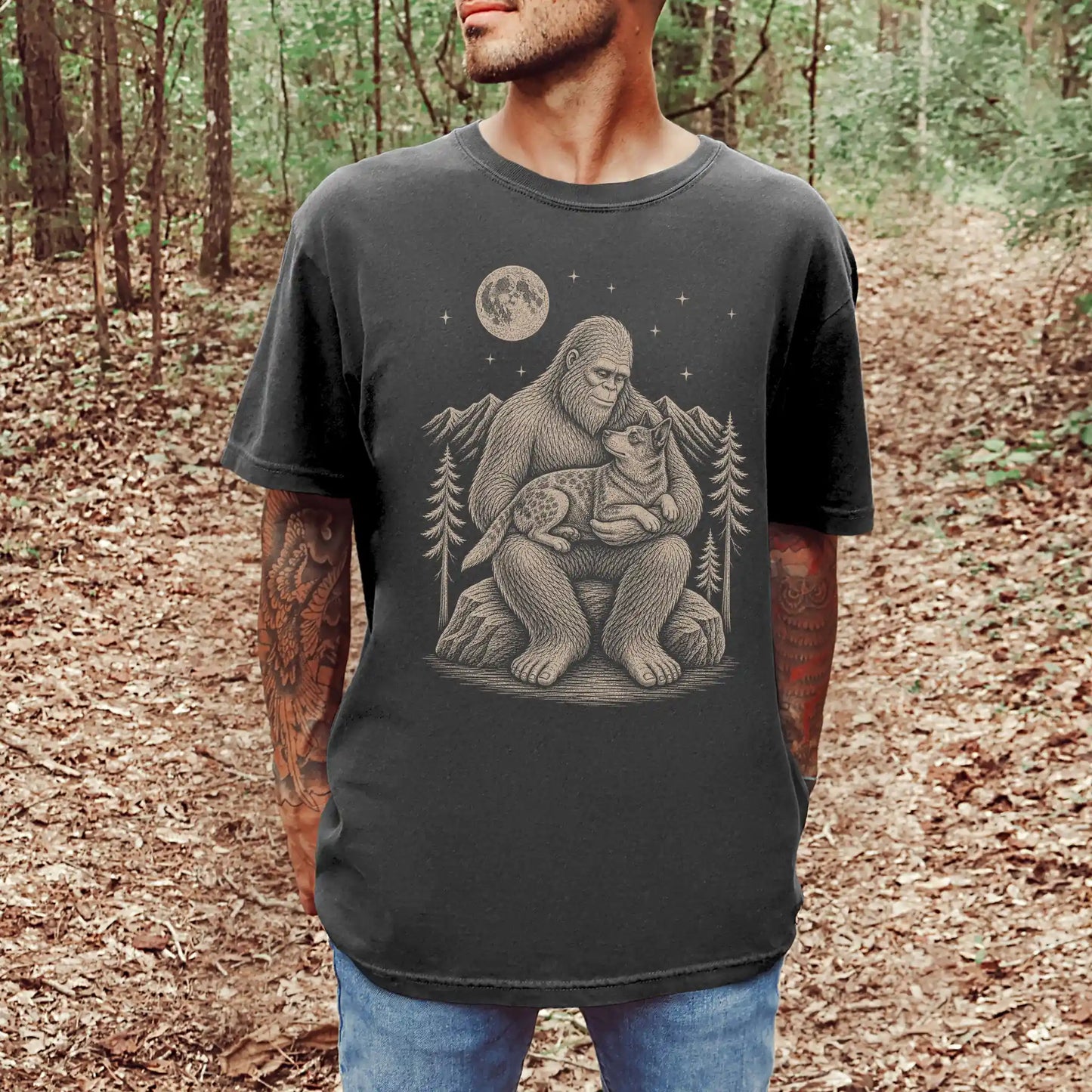 Model wearing a Pepper Comfort Colors® T-shirt showing Bigfoot holding a Blue Heeler