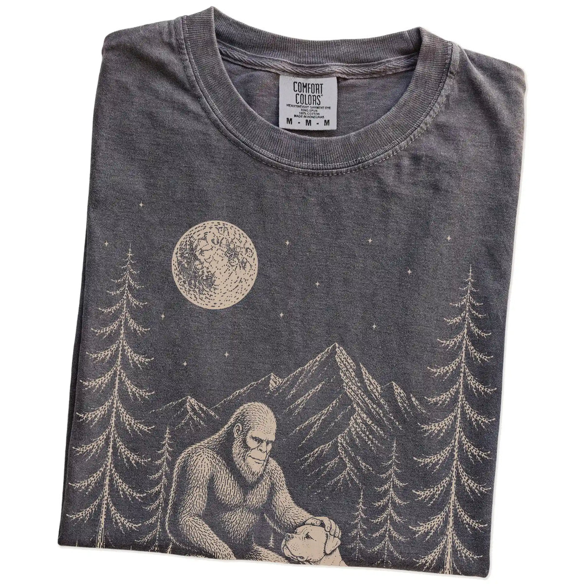 Folded Pepper Comfort Colors® T-shirt showing bigfoot petting a american bulldog beneath the moon in a pine forest