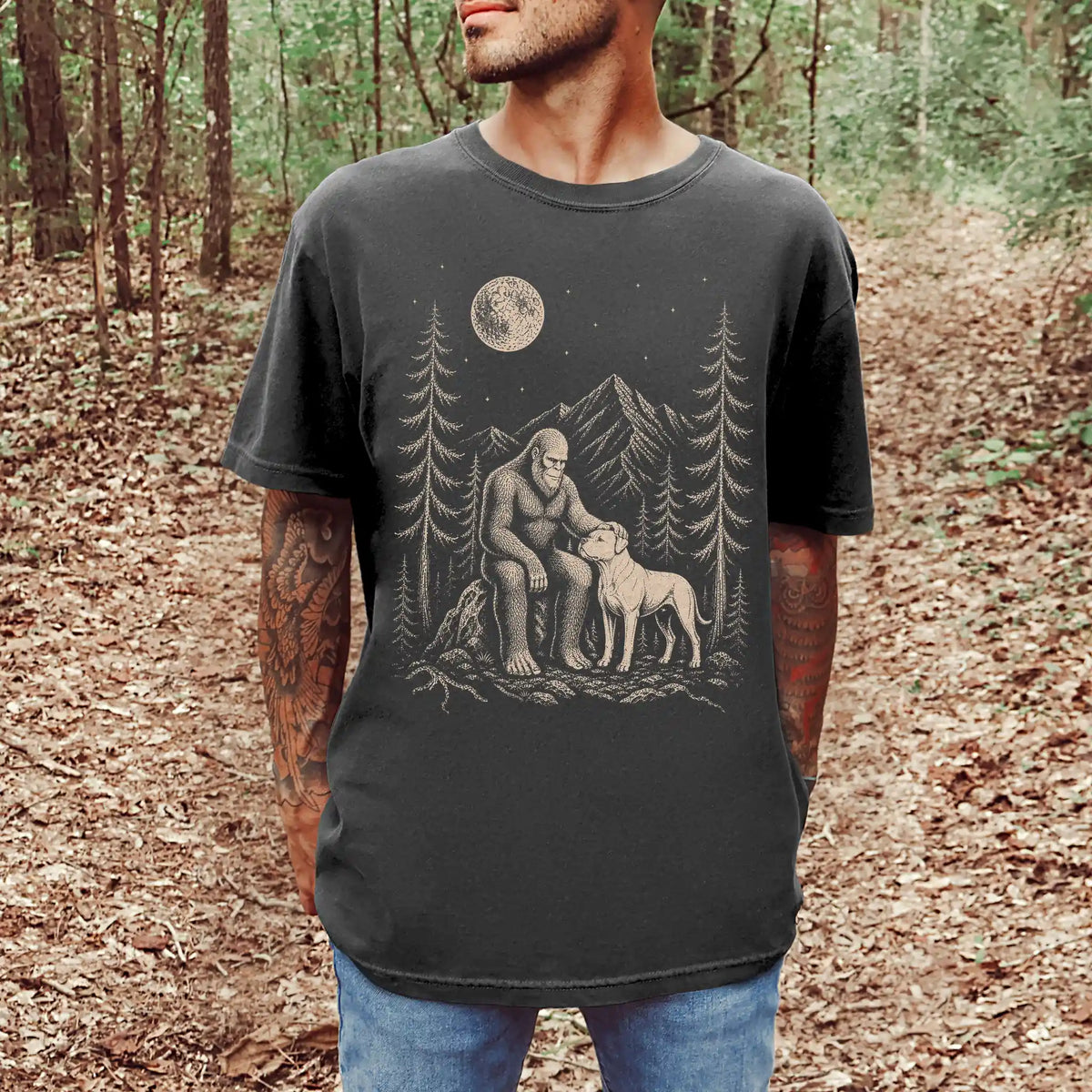 Model wearing a Pepper Comfort Colors® T-shirt with bigfoot petting a american bulldog beneath the moon in a pine forest