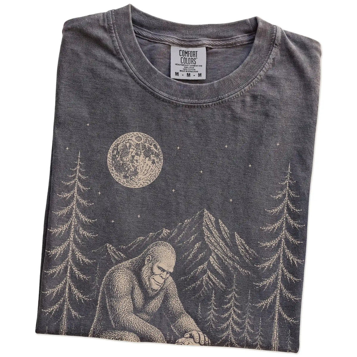 Folded Pepper Comfort Colors® T-shirt showing bigfoot petting a bulldog beneath the moon in a pine forest