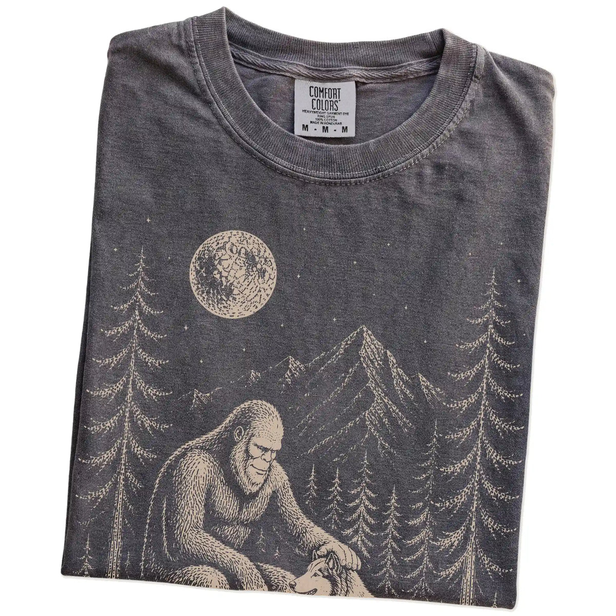 Folded Pepper Comfort Colors® T-shirt showing bigfoot petting a collie beneath the moon in a pine forest