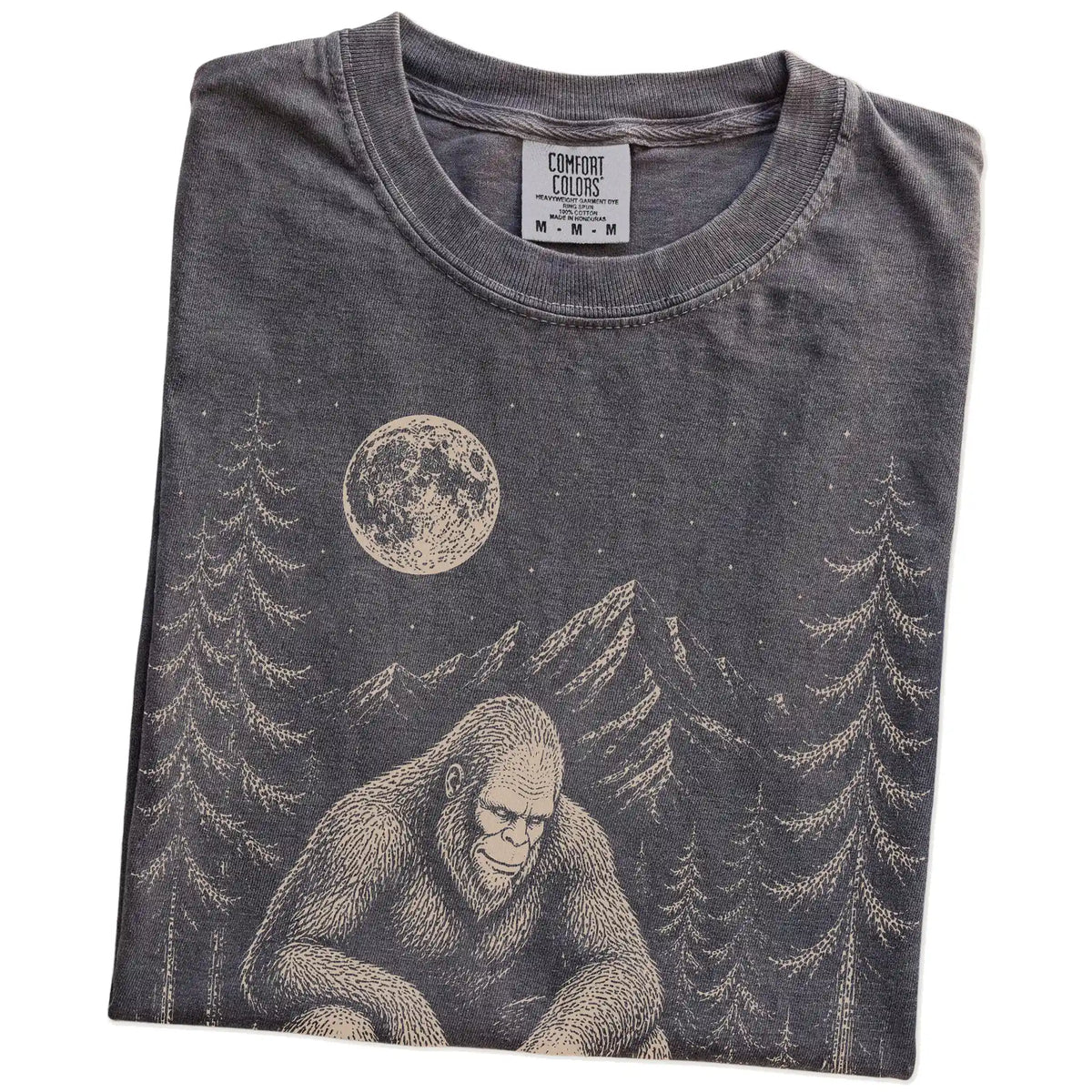 Folded Pepper Comfort Colors® T-shirt showing bigfoot petting a dachshund beneath the moon in a pine forest