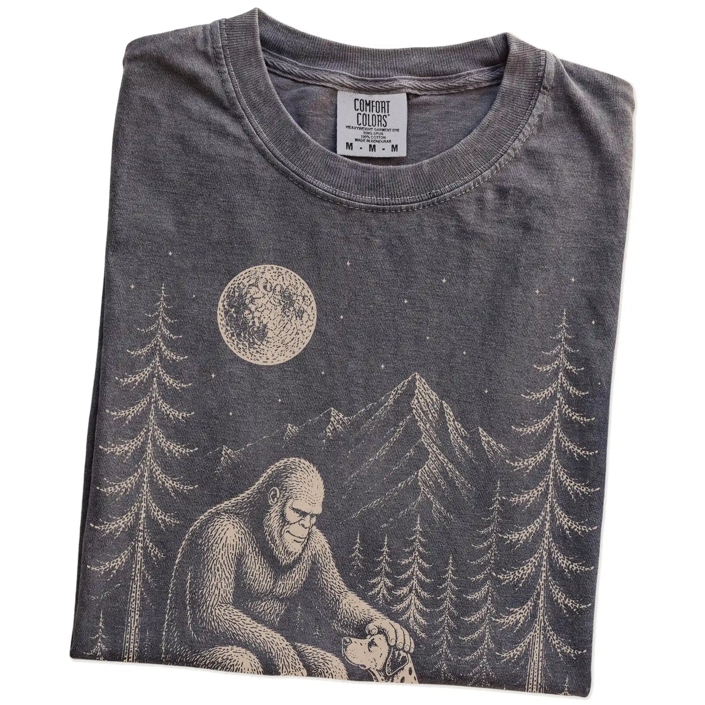 Folded Pepper Comfort Colors® T-shirt showing bigfoot petting a dalmatian beneath the moon in a pine forest