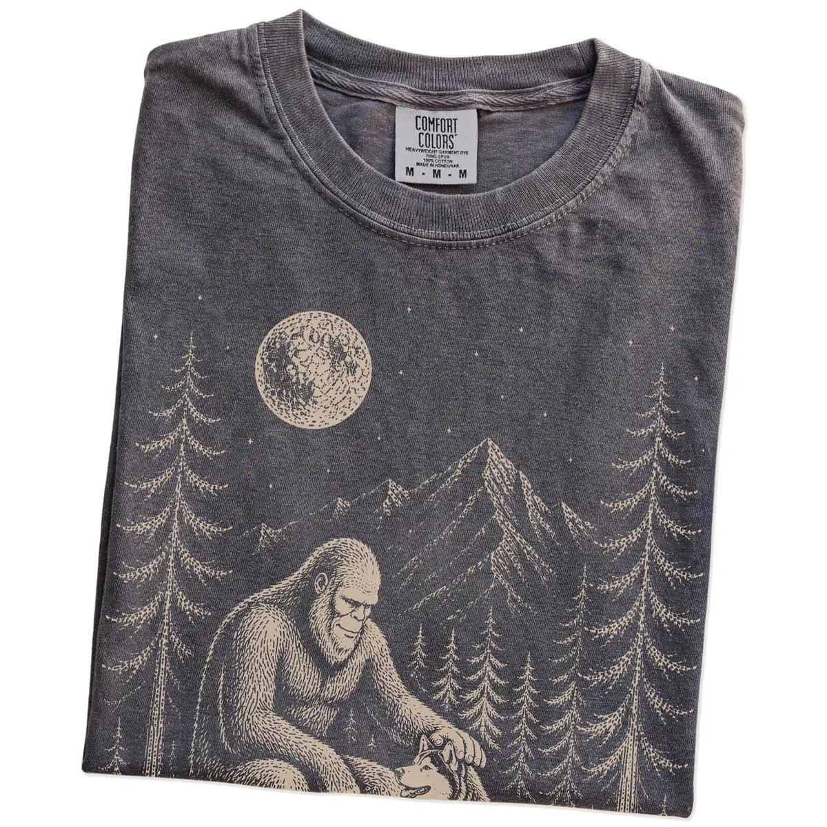 Folded Pepper Comfort Colors® T-shirt showing bigfoot petting a husky beneath the moon in a pine forest