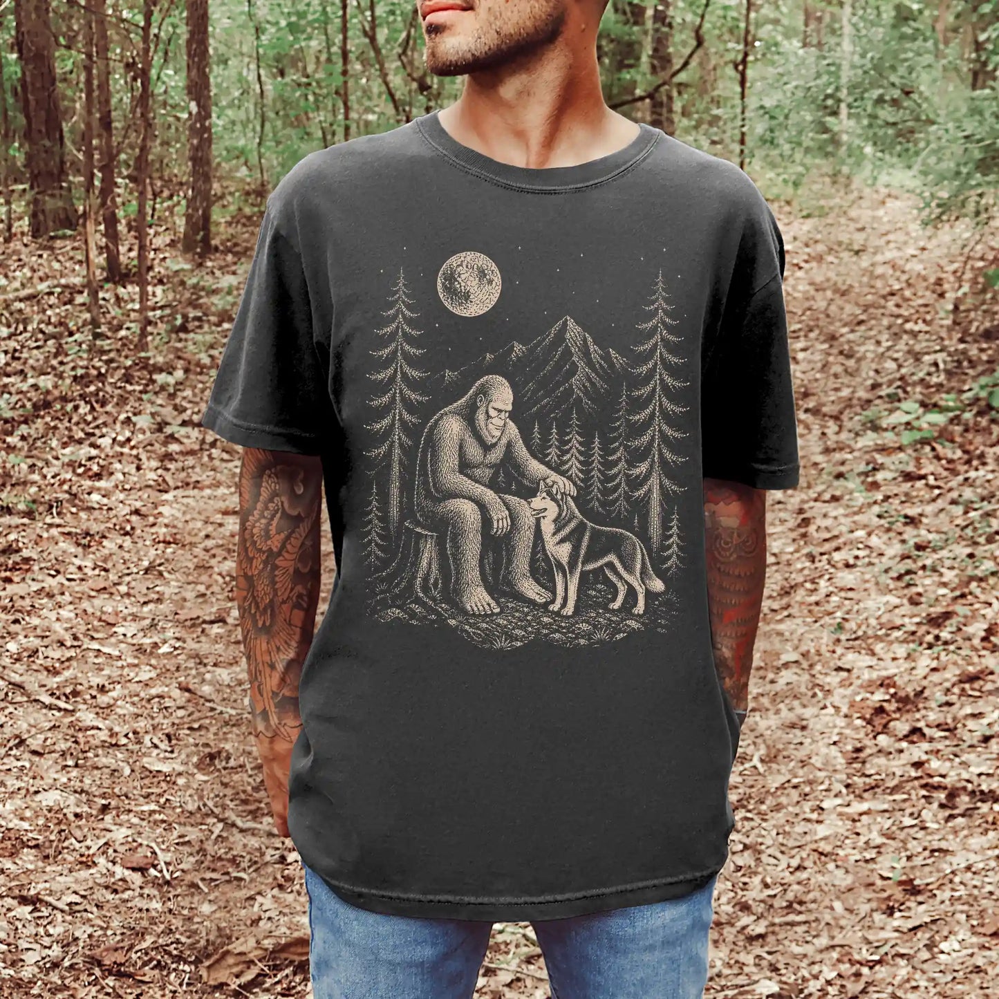Model wearing a Pepper Comfort Colors® T-shirt with bigfoot petting a husky beneath the moon in a pine forest