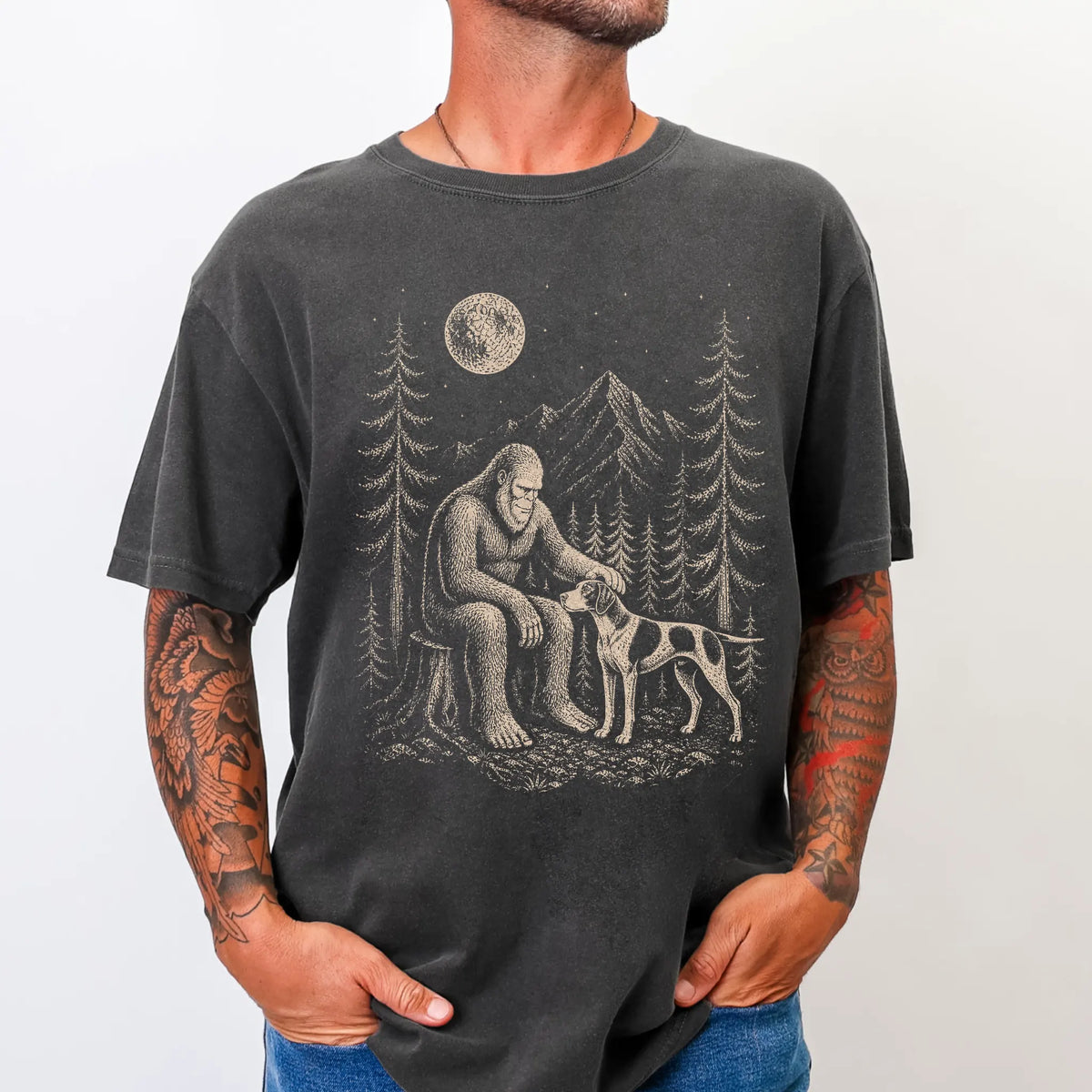 Model wearing a Pepper Comfort Colors® T-shirt with bigfoot petting a pointer beneath the moon in a pine forest