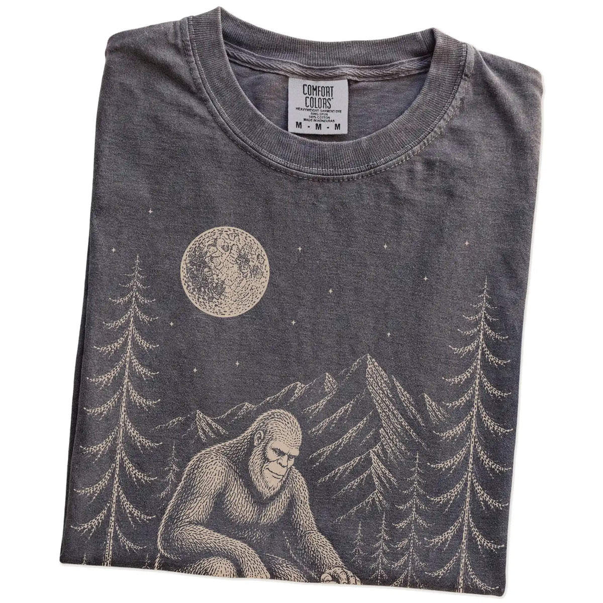 Folded Pepper Comfort Colors® T-shirt showing bigfoot petting a shih tzu beneath the moon in a pine forest