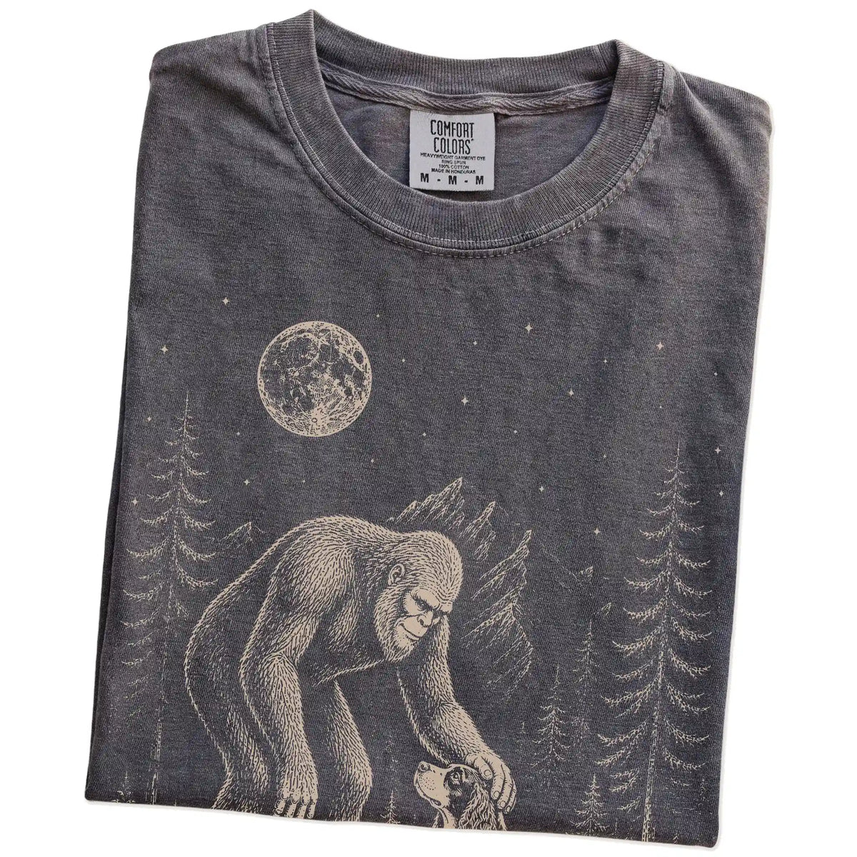 Folded Pepper Comfort Colors® T-shirt showing bigfoot petting a springer spaniel beneath the moon in a pine forest