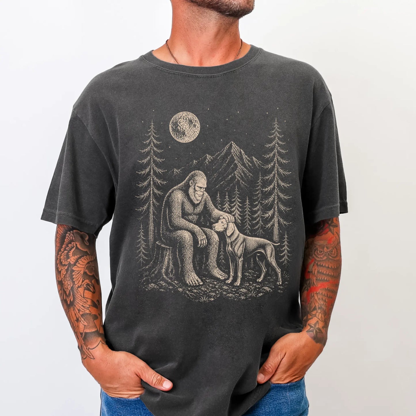Model wearing a Pepper Comfort Colors® T-shirt with bigfoot petting a weimaraner beneath the moon in a pine forest